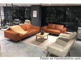 The image shows a modern living room with a large sectional sofa in the center. The sofa is made of orange leather and has a...