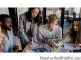 The image shows a group of five young people sitting around a table in a meeting room. They are all dressed in business attir...