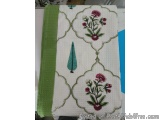 The image is of a white fabric with a green border. The fabric has a floral design on it. The design is made up of three over...