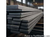 The image shows a stack of black metal bars in a warehouse. The bars are arranged in a horizontal manner and are stacked on t...