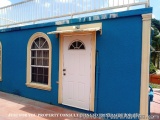 The image shows a small blue building with a white door and two arched windows on the left side. The building appears to be a...