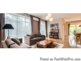 The image shows a modern living room with a large window on the left side. The window has sheer curtains that let in natural...