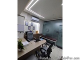 The image shows an office space with a modern design. The room has a white wall with a large window on the right side, which...