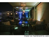 The image shows a dimly lit outdoor seating area at night. The seating area is furnished with black wicker sofas and armchair...