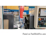 The image shows a CNC (Computer Numerical Control) machine in a workshop. The machine is a large, industrial-looking machine...