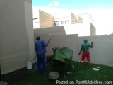 The image shows two men working on a concrete wall. They are standing on a grassy area with a concrete structure in the backg...
