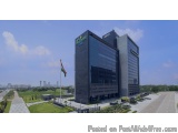 The image shows a modern office building with a glass facade. The building is located on a street with a road in front of it....