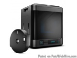 The image shows a black 3D printer with a roll of film next to it. The printer has a sleek and modern design with a large scr...