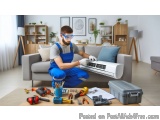In this image, we can see a man wearing blue overalls and safety goggles, working on an air conditioning unit in a living roo...