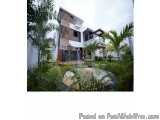 The image shows a modern two-story building with a white exterior and a wooden facade. The building is surrounded by a well-m...