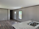 The image shows an empty room with a kitchenette in the foreground. The walls are painted in a light grey color and the floor...