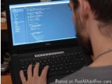 The image shows a man sitting at a desk with a laptop in front of him. The laptop screen is displaying a code snippet with a...