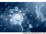 The image shows a person's hand holding a smartphone with the word "CRM" on the screen. The background is a dark blue color w...