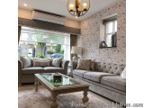 The image shows a modern living room with a large window on the left side. The window has a white brick wall and a chandelier...