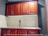 The image shows a kitchen with wooden cabinets and a white countertop. The cabinets are made of wood and have a dark brown fi...