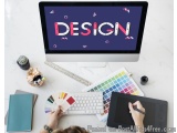 The image shows a desk with a computer monitor displaying the word "DESIGN" in bold, colorful letters on a dark purple backgr...