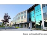 The image shows a modern office building with a glass facade. The building is located on a street with a tree on the left sid...