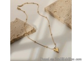 The image shows a gold necklace with a small heart pendant hanging from a thin gold chain. The necklace is resting on a white...