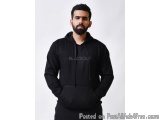The image is a portrait of a young man wearing a black hoodie. He has a beard and is standing with his hands in his pockets....