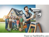 The image shows a group of people standing in front of a house. The house is a two-story building with a sloping roof and a c...