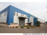 The image shows a large industrial building with a blue and white color scheme. The building has a flat roof and a large gara...