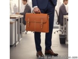 The image shows a man in a blue suit holding a brown briefcase in his hand. He is standing in an office with other people in...