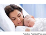The image shows a young woman sleeping with her newborn baby. The woman is lying on her side with her eyes closed and her hea...