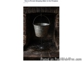 The image shows a metal bucket hanging from a hook in a fireplace. The bucket is filled with water and is being dripped from...