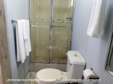 The image shows a small bathroom with a white toilet and a glass shower door. The shower door is made of glass and has a silv...