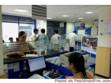 The image shows a reception area of a bank. There are several people in the image, including a woman sitting at a desk with a...