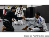 The image shows two men in a martial arts class. The man on the left is wearing a black jiu-jitsu suit and is kneeling on the...