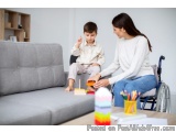 The image shows a mother and her young son sitting on a gray couch in a living room. The mother is sitting on the armrest of...