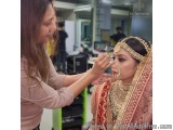 The image shows a young woman getting her makeup done by a makeup artist. The makeup artist is applying makeup to the bride's...