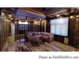 The image shows a modern living room with a wooden floor and walls. The room has a high ceiling with a unique design that has...