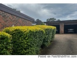 The image shows a brick building with a garage on the right side. The garage is covered with a black roof and has a car parke...