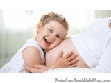 The image shows a young girl, probably around 2-3 years old, lying on her stomach with her mother. The girl is wearing a whit...