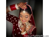 The image is a portrait of a beautiful Indian bride. She is wearing a traditional red and gold lehenga with intricate gold em...