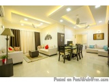 The image shows a modern and luxurious living room and dining area. The room has a high ceiling with recessed lighting and a...
