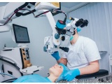 The image shows a dental clinic with a patient lying on a dental chair with a dental examination table in front of them. The...