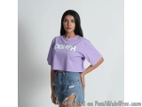 The image shows a young woman standing in front of a plain white background. She is wearing a purple cropped t-shirt with the...