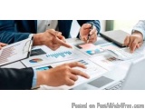 The image shows a group of people sitting around a table with papers and graphs spread out in front of them. The papers appea...