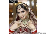 The image is a portrait of a beautiful Indian bride. She is wearing a traditional red and gold bridal outfit with a matching...