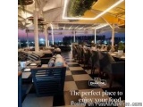 The image shows the interior of a restaurant with a beautiful view of the city at night. The restaurant has a modern and eleg...
