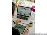 The image shows a person sitting at a desk with a laptop and a tablet in front of them. The laptop is open and the screen is...