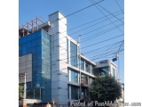 The image shows a modern building with a blue glass facade. The building is located on a street corner with a few other build...