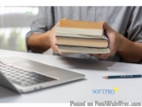 The image shows a person's hands holding a stack of books. The books are of different sizes and colors, with the topmost book...