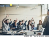 The image shows a group of people in a conference room with their hands raised in the air. They are all smiling and appear to...