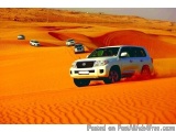 The image shows a group of four cars driving through a desert landscape. The car in the foreground is a white Toyota Land Cru...