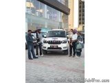 The image shows a group of people standing in front of a white SUV. The SUV appears to be a Mahindra Bolero, as indicated by...