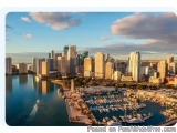 The image is an aerial view of a city skyline with a harbor in the foreground. The city is Miami, Florida, United States. The...